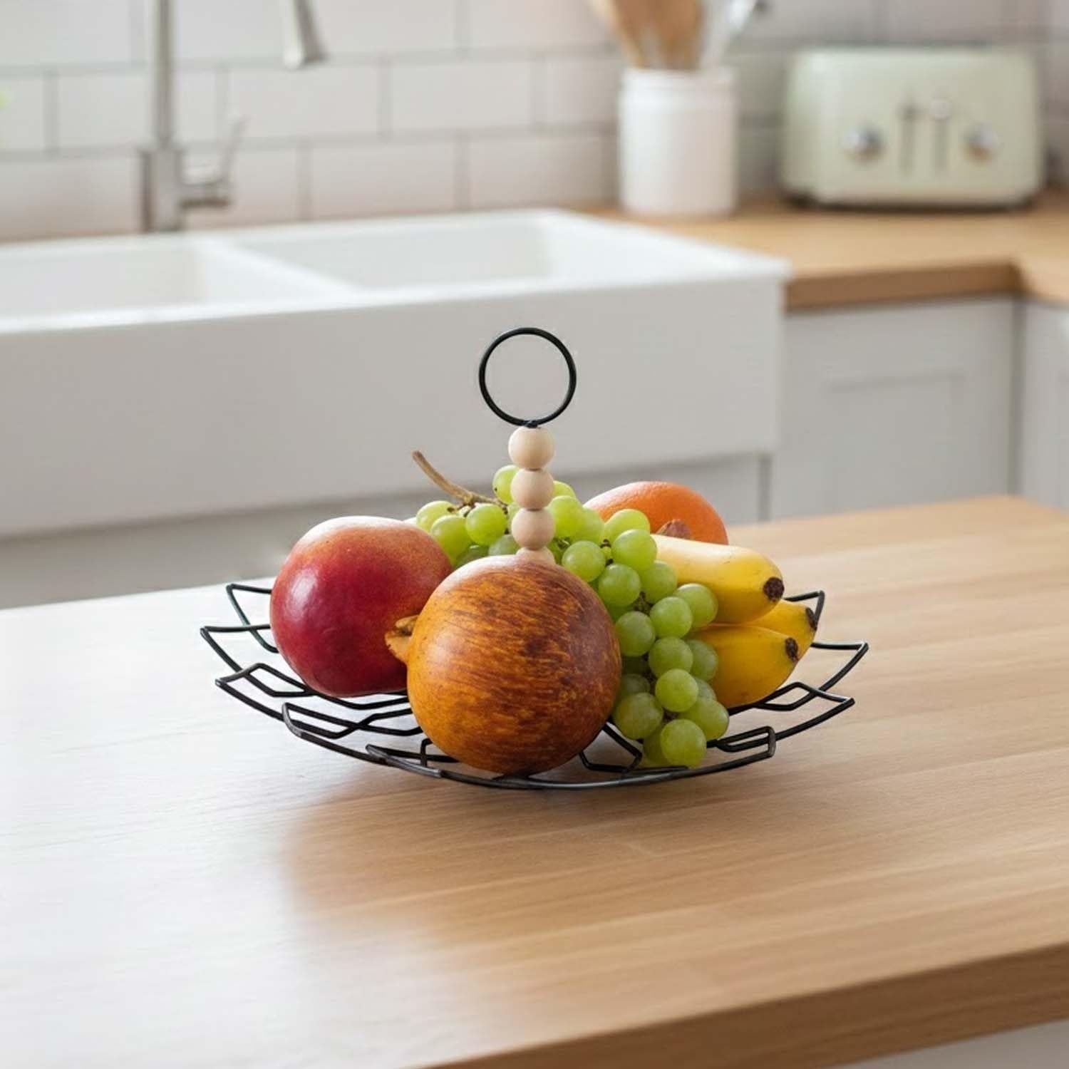 Go Hooked black metal 2-tier fruit basket with wooden beads and ring handle, filled with apples, grapes, bananas, and oranges.