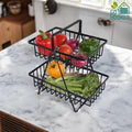 GoHooked black metal 2-tier fruit basket with handle, holding various vegetables and fruits on a marble countertop.