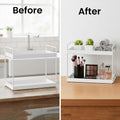GoHooked white 2-tier iron countertop organizer holding makeup brushes, eyeshadow palette, perfume bottles, small plants, and rolled towels.