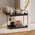 GoHooked black 2-tier iron countertop organizer holding makeup brushes, eyeshadow palette, lotions, perfumes, and small plants.