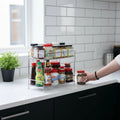 GoHooked 2-tier stainless steel multipurpose shelf basket with spice jars and toiletries on a kitchen counter.
