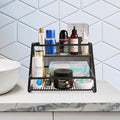 GoHooked black 2-tier metal vanity rack organizer holding various bathroom products and toiletries on a countertop.