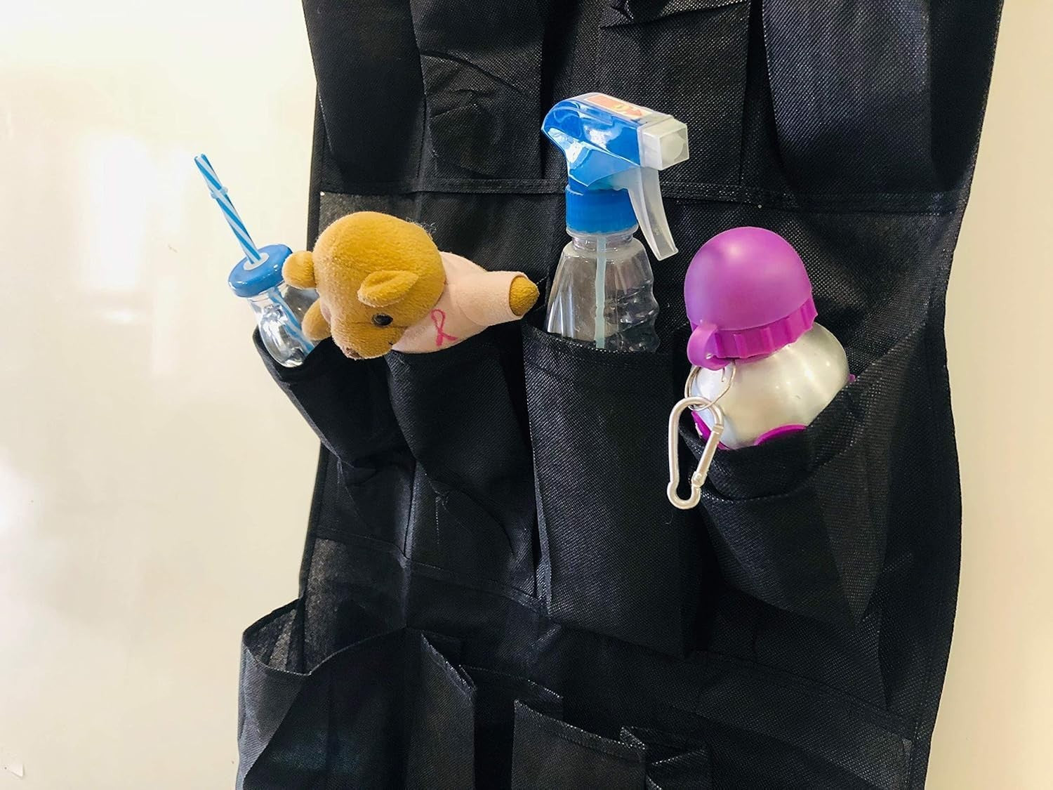 GoHooked black non-woven fabric 20-pocket over-the-door organizer with clear pockets holding a teddy bear, bottle, and spray bottle.