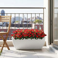 Go Hooked 24-inch black rectangular polymer planter pot filled with red flowers on a balcony.
