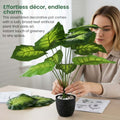 GoHooked artificial Alocasia plant with broad green leaves in a black speckled pot, arranged by a woman at a desk.