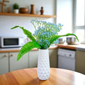 Go Hooked light blue artificial baby's breath flowers in a white textured vase, with green leaves. Realistic floral arrangement for decor.