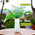 GoHooked light blue artificial baby's breath flowers in a white textured vase, with green fern leaves. Realistic floral arrangement.