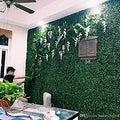GoHooked artificial boxwood hedge grass tiles create a lush green wall with white flowers, ideal for outdoor or indoor decor.