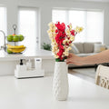 Go Hooked artificial yellow and red flowers in a white textured vase, displayed on a white table.