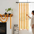 GoHooked orange and yellow artificial marigold flower garlands draped on a fireplace and window for festive decor.