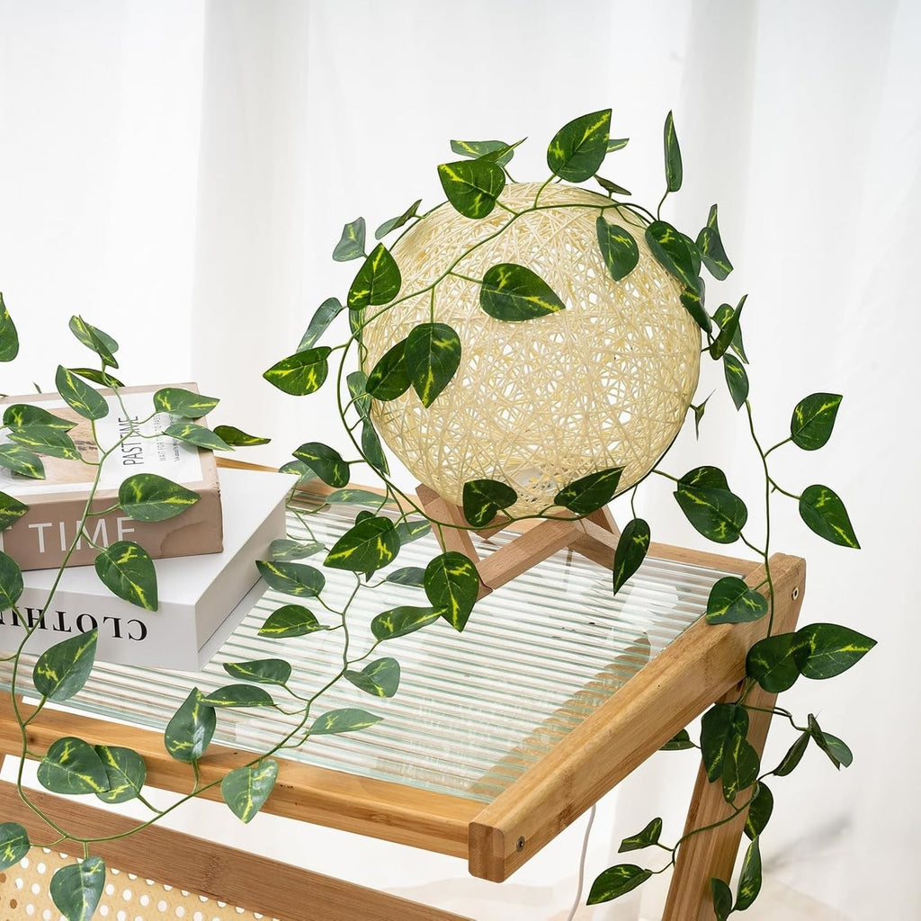 GoHooked artificial money plant creeper draped over a decorative rattan sphere lamp on a wooden side table