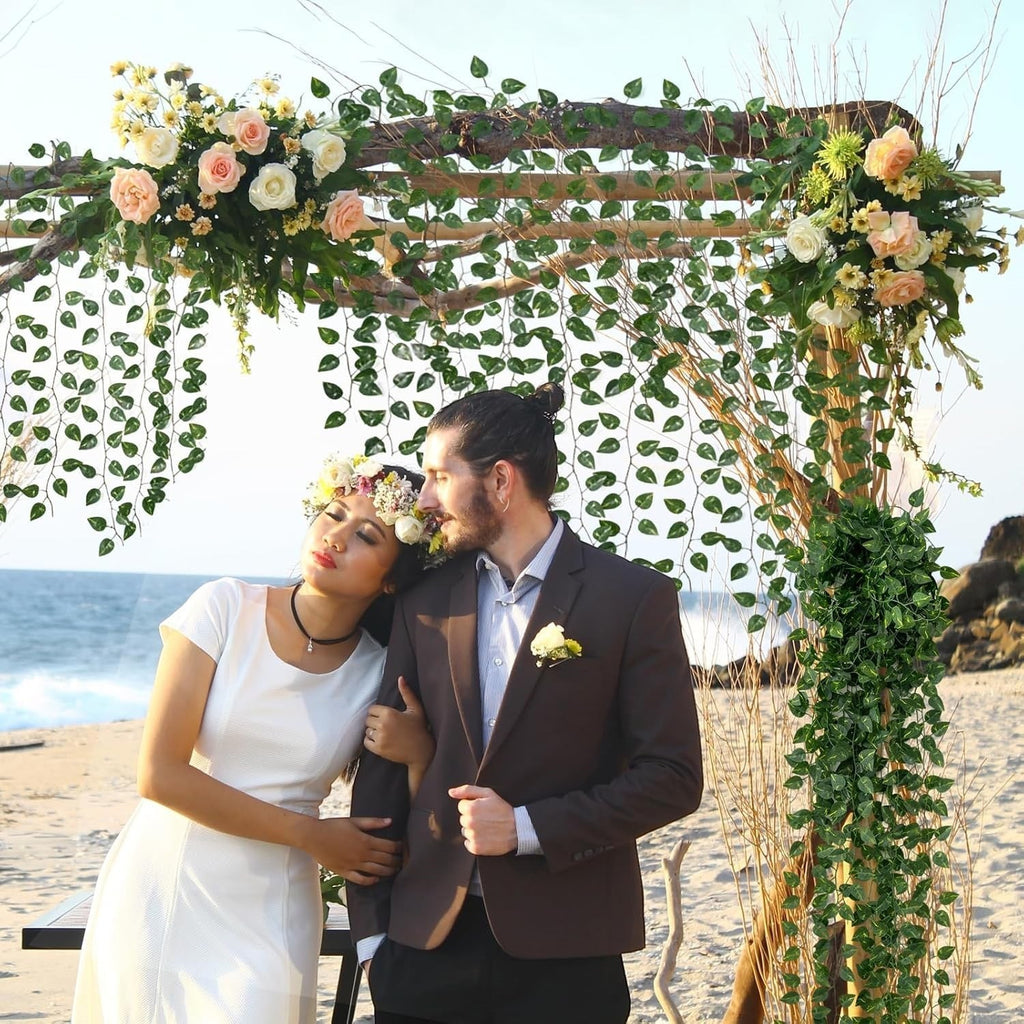 GoHooked artificial money plant leaf garlands decorating a beach wedding arch with a couple posing underneath