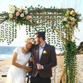 GoHooked artificial money plant leaf garlands decorating a beach wedding arch with a couple posing underneath
