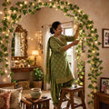 GoHooked artificial money plant leaf garland with fairy lights draped over a home doorway, styled by a woman.
