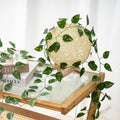 GoHooked artificial money plant leaf garland draped over a decorative rattan orb lamp on a wooden table.