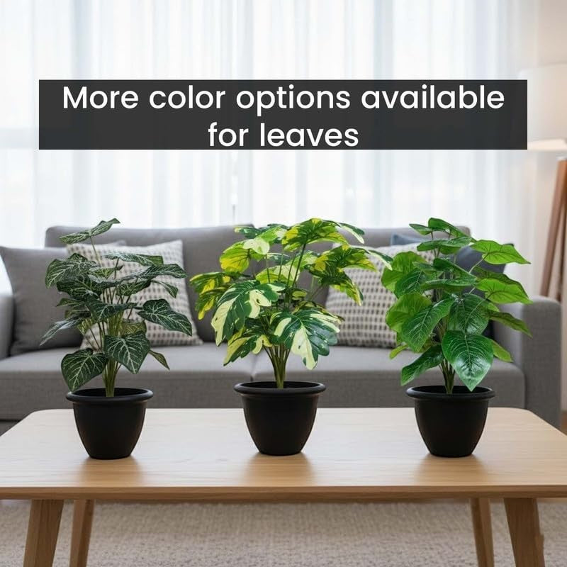 GoHooked artificial plants with variegated and green leaves in black pots on a table in front of a sofa.