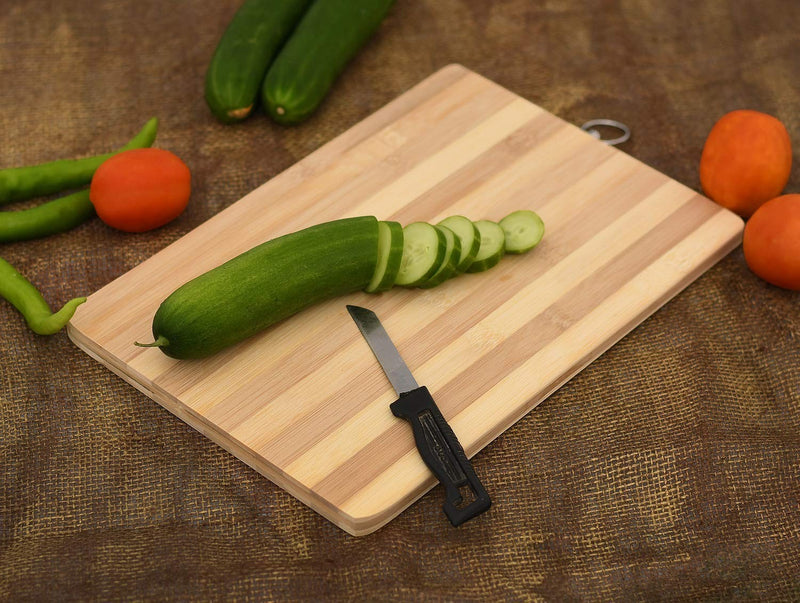 Go Hooked natural bamboo cutting board with a sliced cucumber and knife. Includes tomatoes and green peppers.