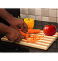 GoHooked bamboo cutting board with striped pattern, being used to slice carrots. Yellow bell pepper and tomato visible.