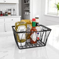 GoHooked BIANCO Twist black wire storage basket with handles, holding condiments like pickles, mustard, and hot sauce.