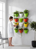 GoHooked Bianco wall hanging pots in assorted colors (green, orange, yellow, white) holding plants. Woman watering plants.