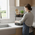 Go Hooked black 2-tier metal mesh rotating countertop storage basket with jars, utensils, and plant.