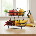 GoHooked black metal 2-tier fruit basket with apples, mango, grapes, and bananas on a wooden table.