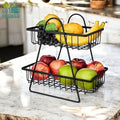 GoHooked black metal 2-tier fruit basket holding apples, bananas, oranges, and grapes on a kitchen counter.