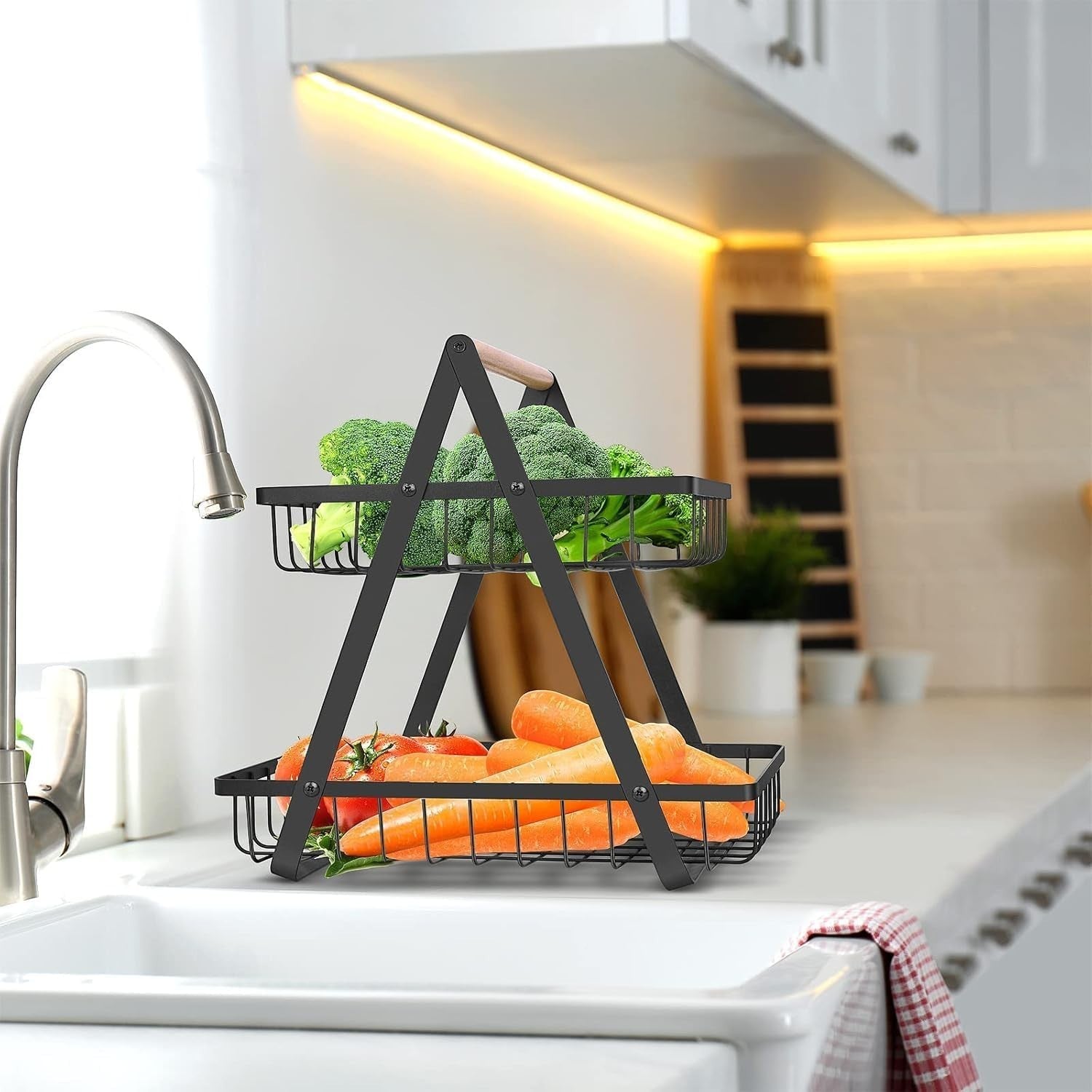 Go Hooked black metal 2-tier storage basket with wooden handle, holding broccoli, tomatoes, and carrots.