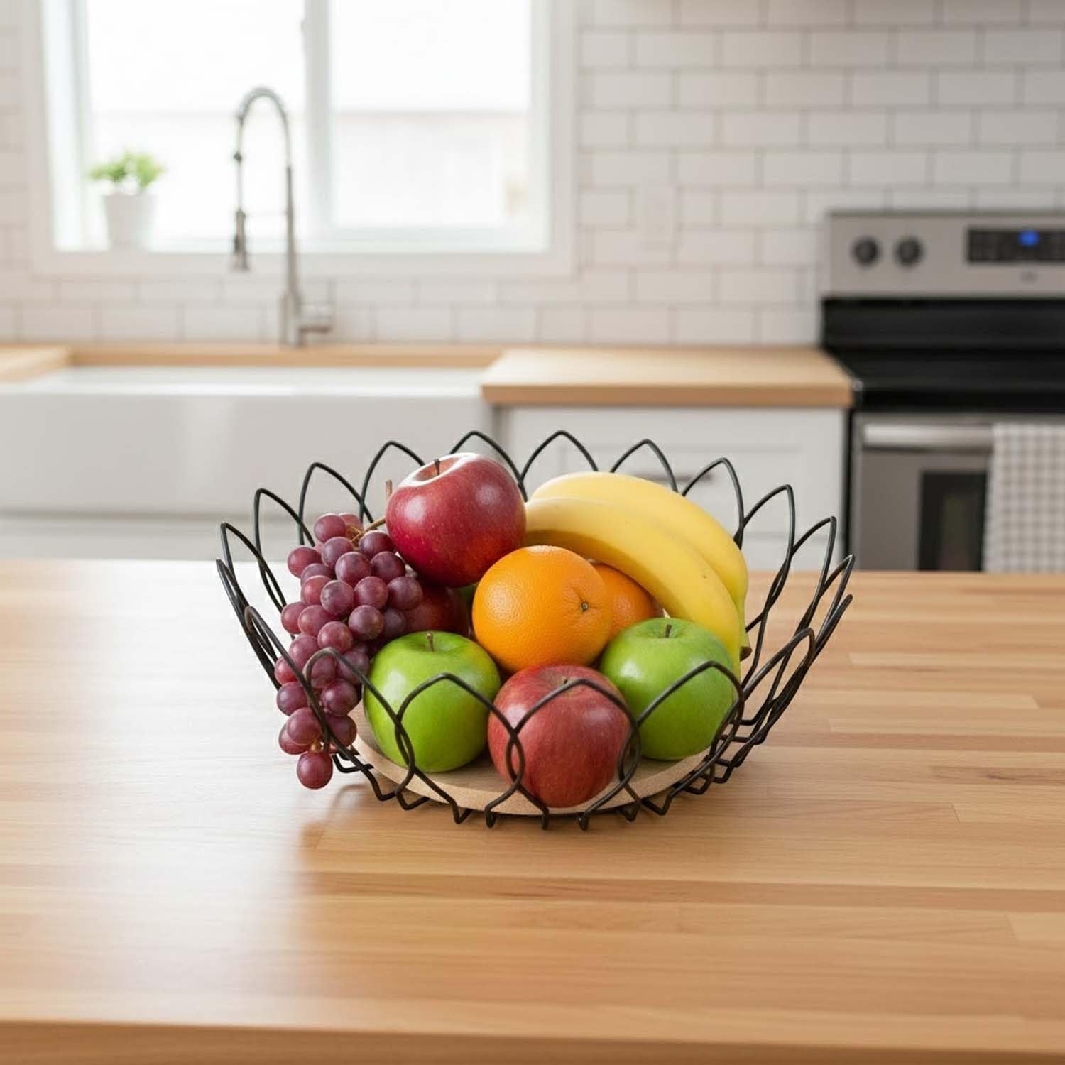 Go Hooked black metal wire fruit basket with a decorative petal edge, filled with apples, bananas, oranges, and grapes.