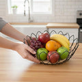 Go Hooked black metal wire fruit basket with wooden base, holding apples, bananas, oranges, and grapes.