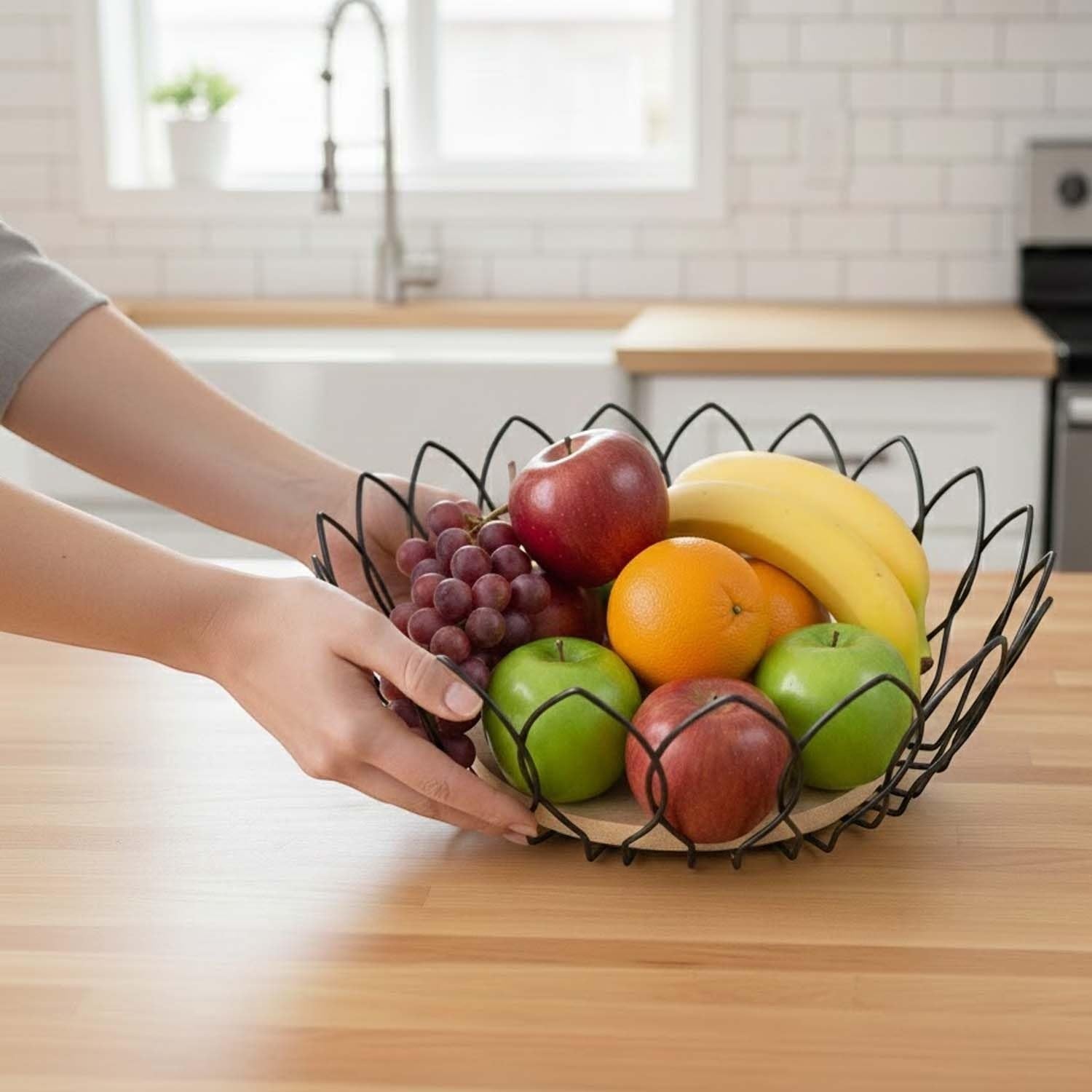 Go Hooked black metal wire fruit basket with wooden base, holding apples, bananas, oranges, and grapes.