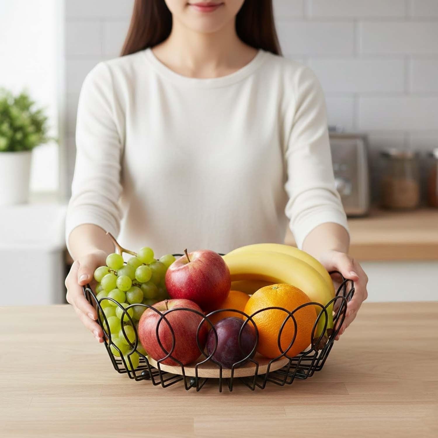 GoHooked black metal wire fruit basket with wooden base, holding apples, bananas, oranges, plums, and grapes.