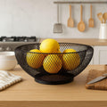 GoHooked black double-layer metal mesh fruit bowl with lemons on a kitchen counter.