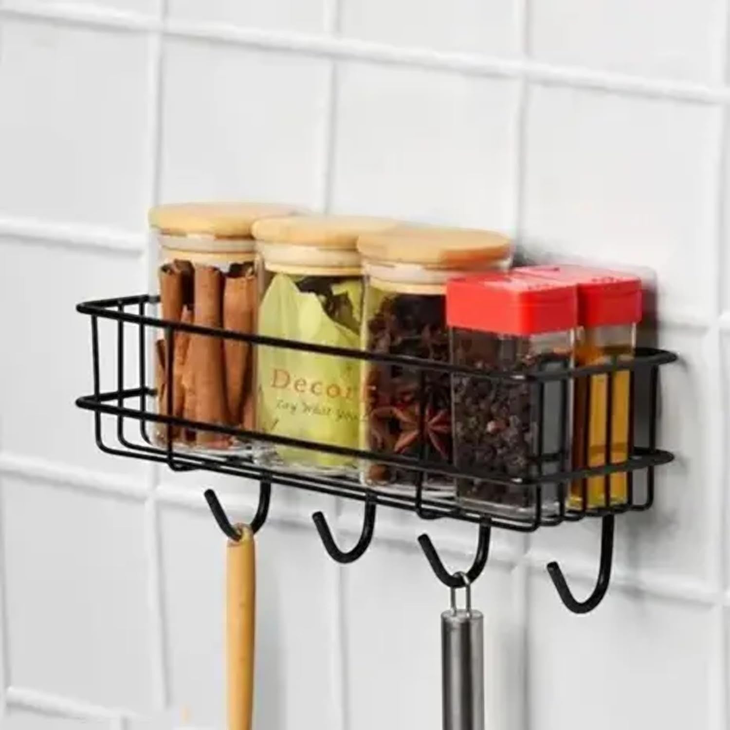 Go Hooked black metal wall-mounted storage basket with hooks, holding spice jars and utensils. No-drill adhesive installation.