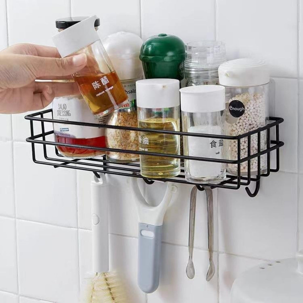 GoHooked black metal wall-mounted storage basket with hooks, holding spice jars and kitchen utensils. No-drill adhesive shelf.