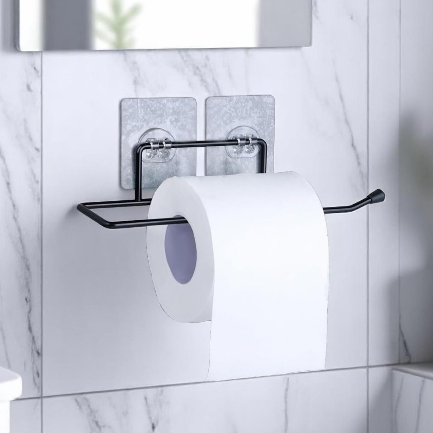 GoHooked black metal self-adhesive toilet paper holder with a roll of toilet paper mounted on a marble-patterned wall.