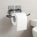 GoHooked black metal self-adhesive toilet paper holder with a roll of white toilet paper attached to a tiled wall.