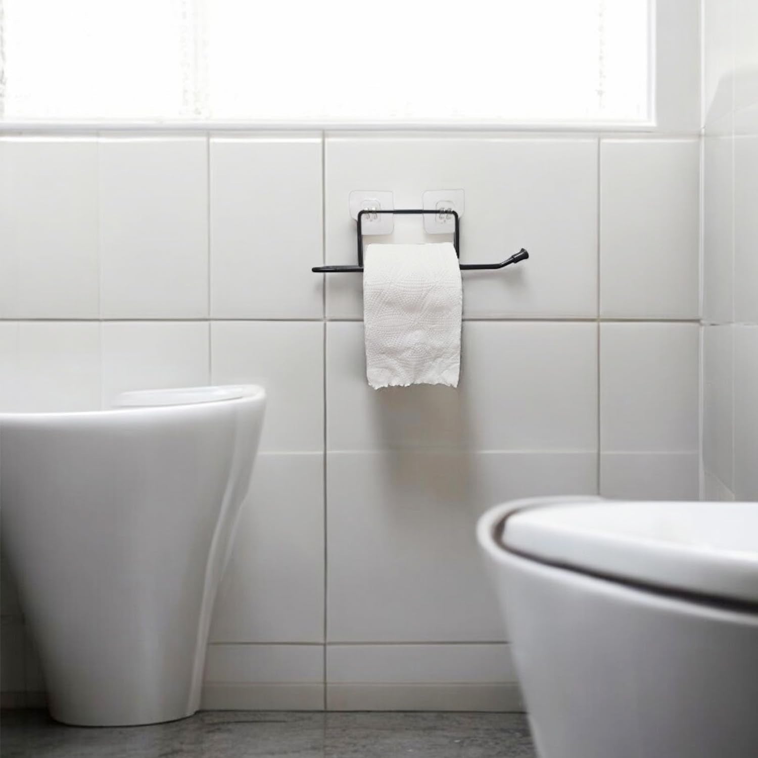 GoHooked black rustproof metal self-adhesive toilet paper holder with a roll of toilet paper mounted on white tiled wall.