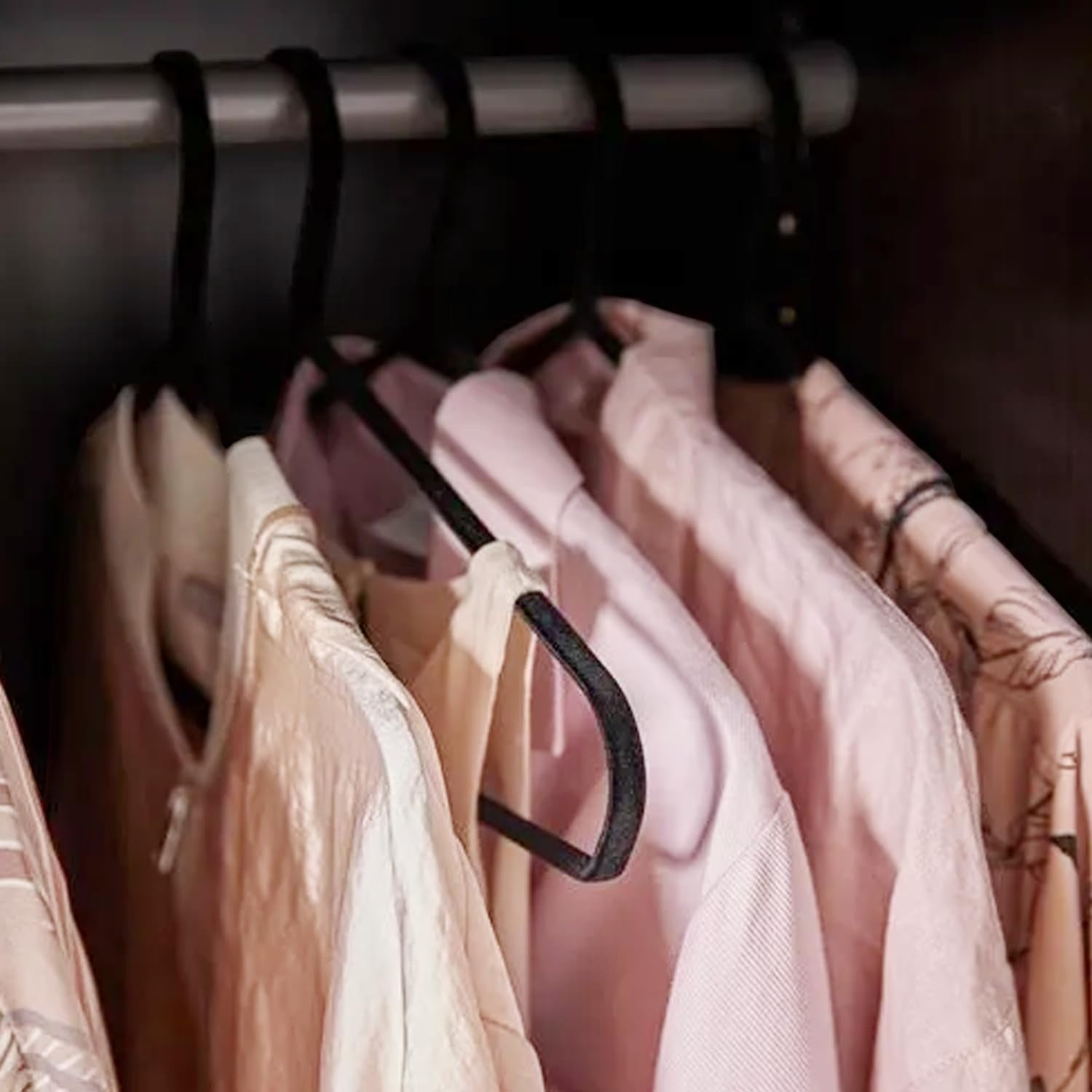 GoHooked black plastic hangers with non-slip grooves holding pink shirts and dresses in a closet.