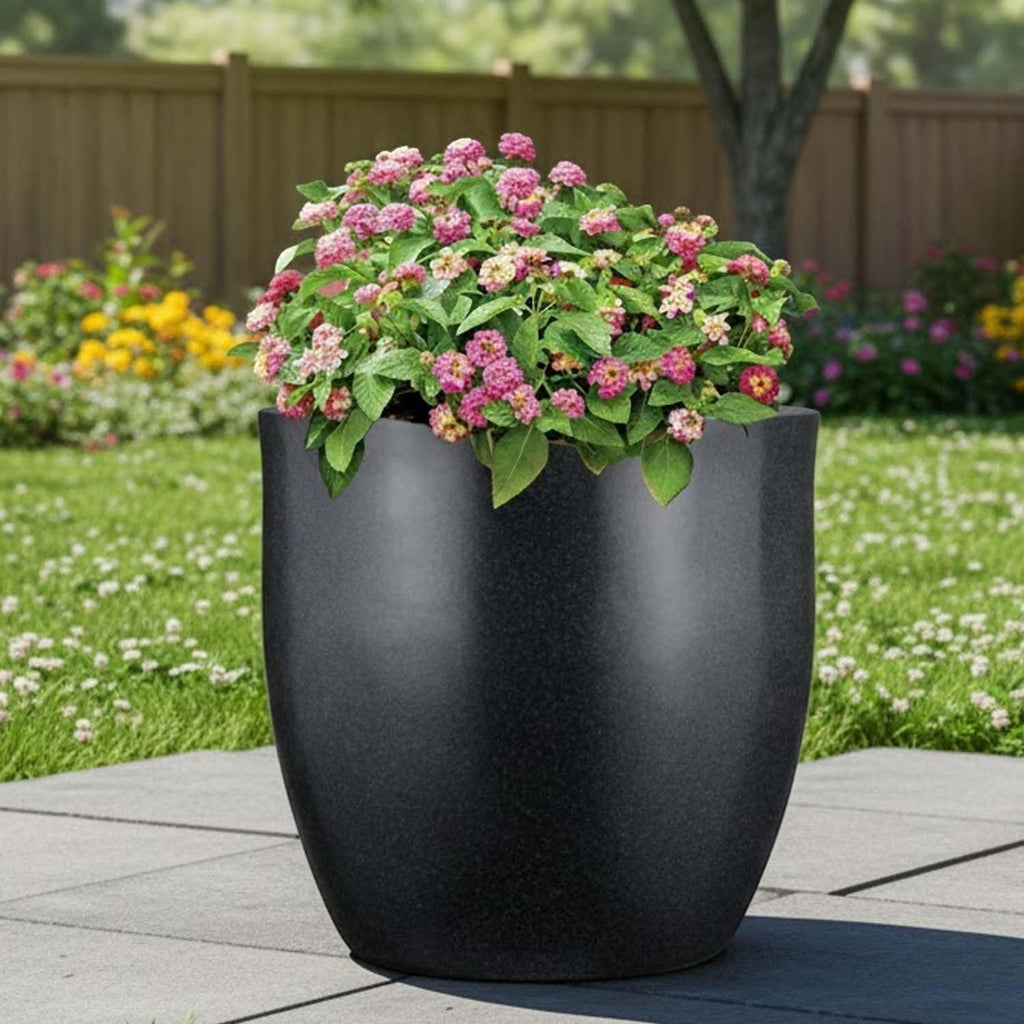 Go Hooked 22-inch black polymer planter with a modern, rounded shape, holding pink flowers. Ideal for indoor or outdoor use.
