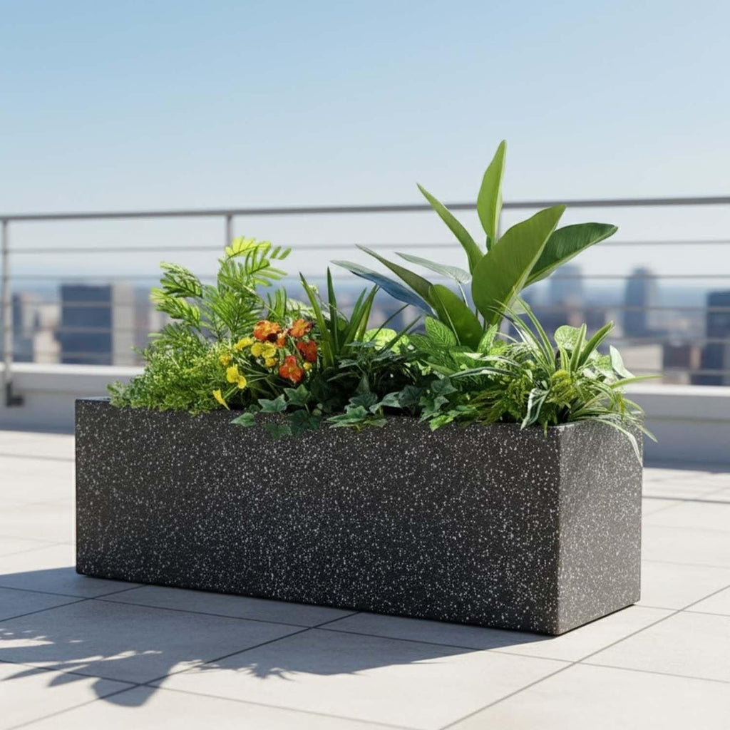 GoHooked rectangular black polymer planter with stone texture, filled with lush green plants on a sunny rooftop balcony.