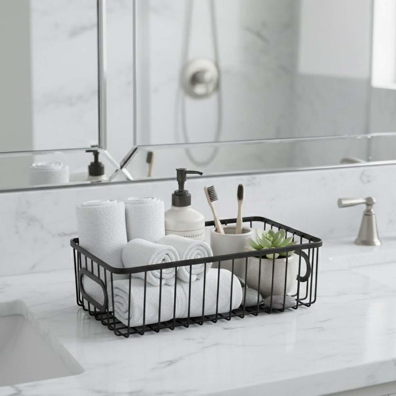 Go Hooked black metal wire storage basket with handles, holding rolled white towels, soap dispenser, toothbrushes, and a small plant.