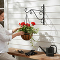 GoHooked black wrought iron hanging planter bracket with decorative scrollwork, holding a basket of red flowers and greenery.