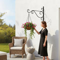 Go Hooked black wrought iron hanging planter bracket with a basket of pink flowers.
