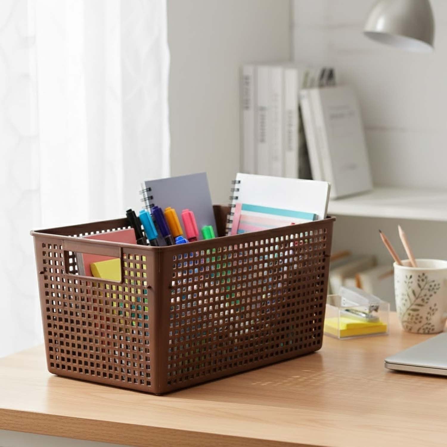 GoHooked brown plastic storage basket with perforated sides, holding notebooks, pens, and sticky notes on a desk.