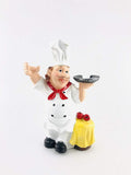 GoHooked white resin chef figurine holding a plate, with a yellow draped table and red apples. Eco-friendly kitchen decor.