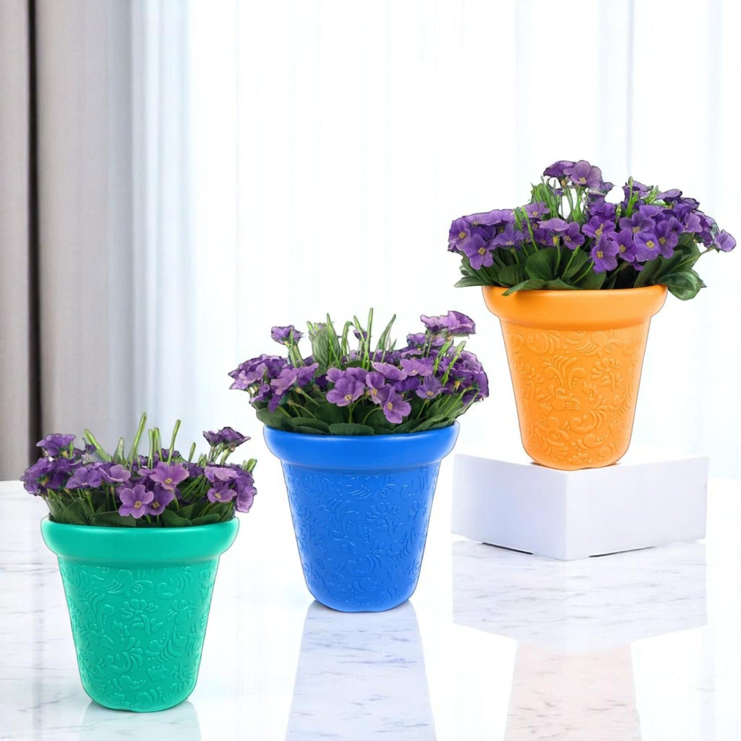 GoHooked set of three colorful embossed plastic planter pots with purple flowers on a white marble surface