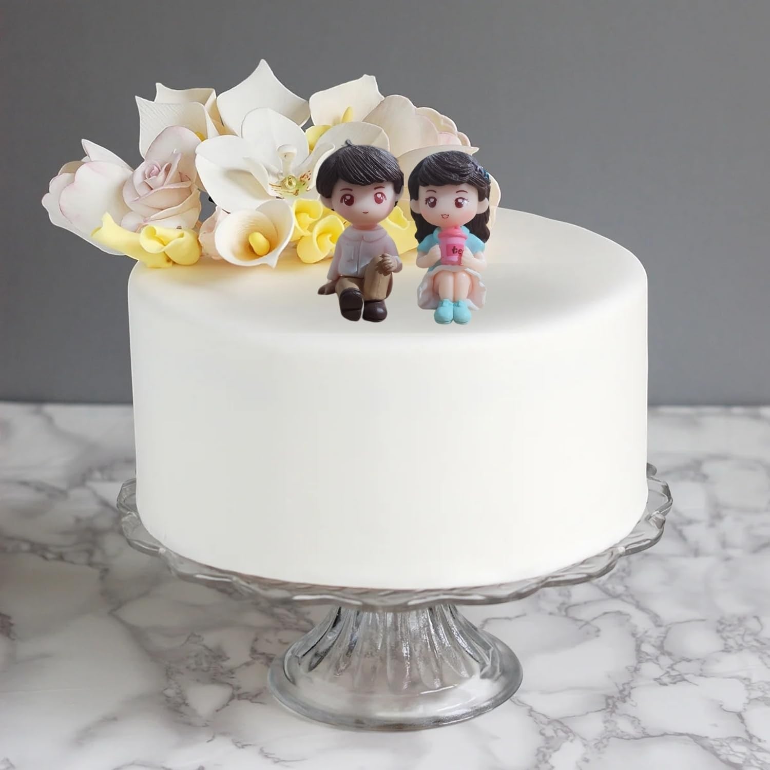 Go Hooked romantic couple figurines sitting on a white cake, one in a blue dress holding a pink cup. Resin material.