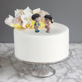 Go Hooked romantic couple figurines in ice cream kids theme, boy in blue, girl in pink, on white cake with floral decor.