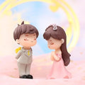 Go Hooked resin couple figurines: groom in grey suit, bride in pink dress, holding flowers. Romantic decor.